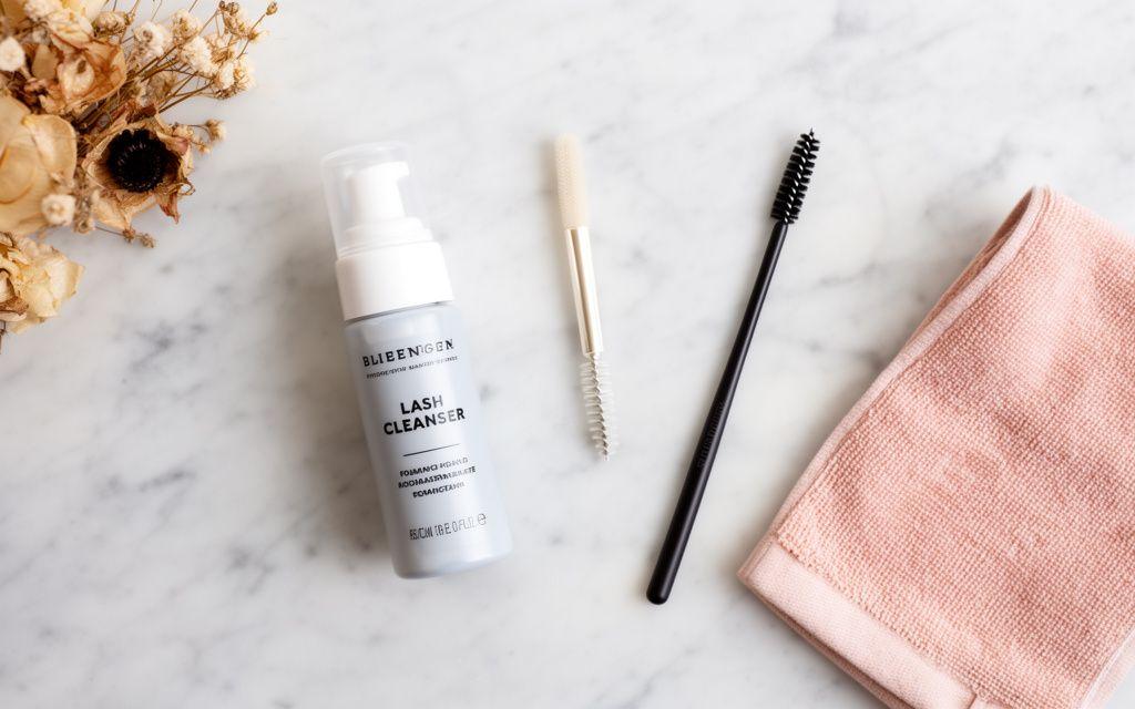 Lash cleanser, soft brush and spoolie laid out on a marble surface
